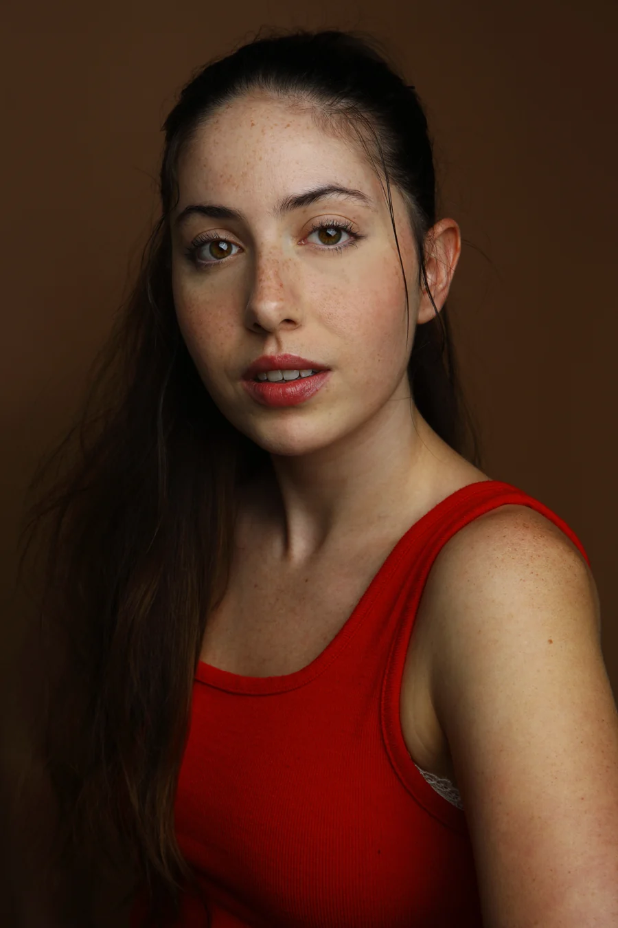 Theatrical headshot in a red top against a dark brown backdrop